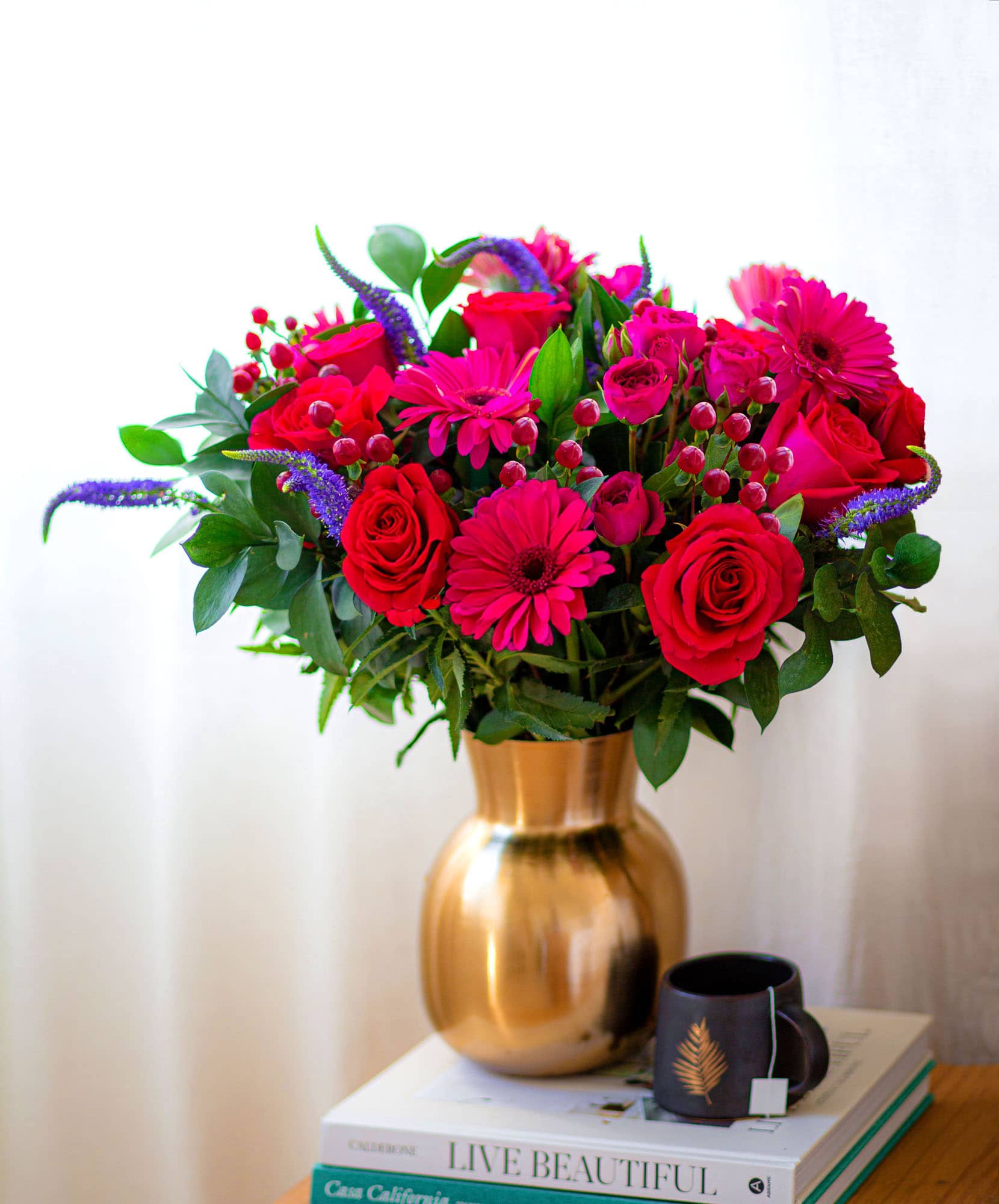 Vibrant bouquet of pink roses, gerbera daisies, and lush greens in a chic golden vase.